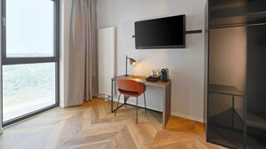 A modern hotel room with a large window, a desk with a lamp, a flat-screen TV, and a built-in wardrobe. - B&B Hotel Berlin Airport-Nord (Berlin)