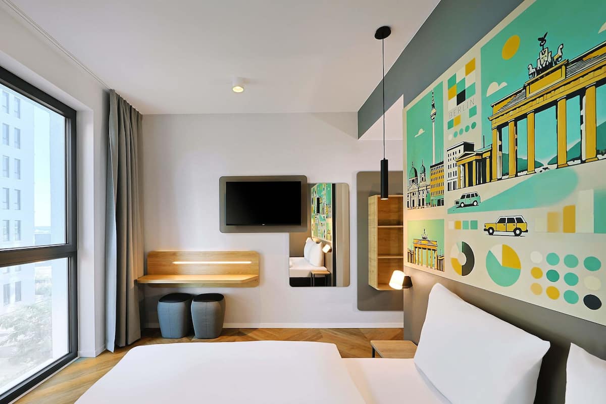 Une chambre d’hôtel moderne dotée d’un grand lit, d’un téléviseur à écran plat, d’un banc en bois et d’une décoration murale sur le thème de la ville.