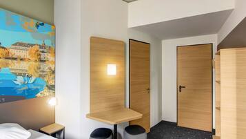 Une chambre d’hôtel moderne équipée d’un lit, d’un bureau, de deux chaises, d’une poubelle et d’un tableau représentant des cygnes sur un mur.