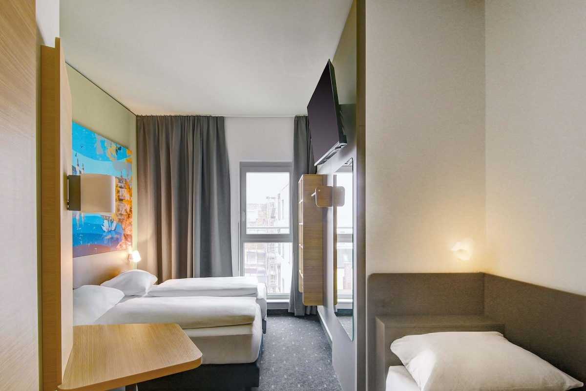 A hotel room with two beds, a small table, a TV, and a window with curtains.