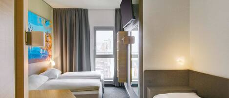 Habitación de hotel con dos camas, una mesita, un televisor y una ventana con cortinas.