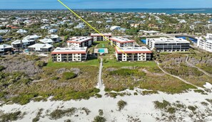 Luftaufnahme eines Hotelkomplexes an der Küste mit mehreren Gebäuden, einem zentralen Innenhof und einem Strand im Vordergrund.