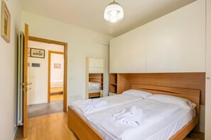 Quarto com cama de madeira, guarda-roupa, espelho e porta que dá para outro cômodo.