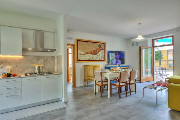 A modern kitchen with white cabinets, a stainless steel range hood, and a dining area with a yellow sofa and a table set for two.