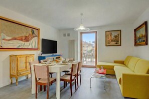 A living room with a dining area, a yellow sofa, and artwork on the walls. - Boutique Terrace Apartment In The Center (Riva del Garda)