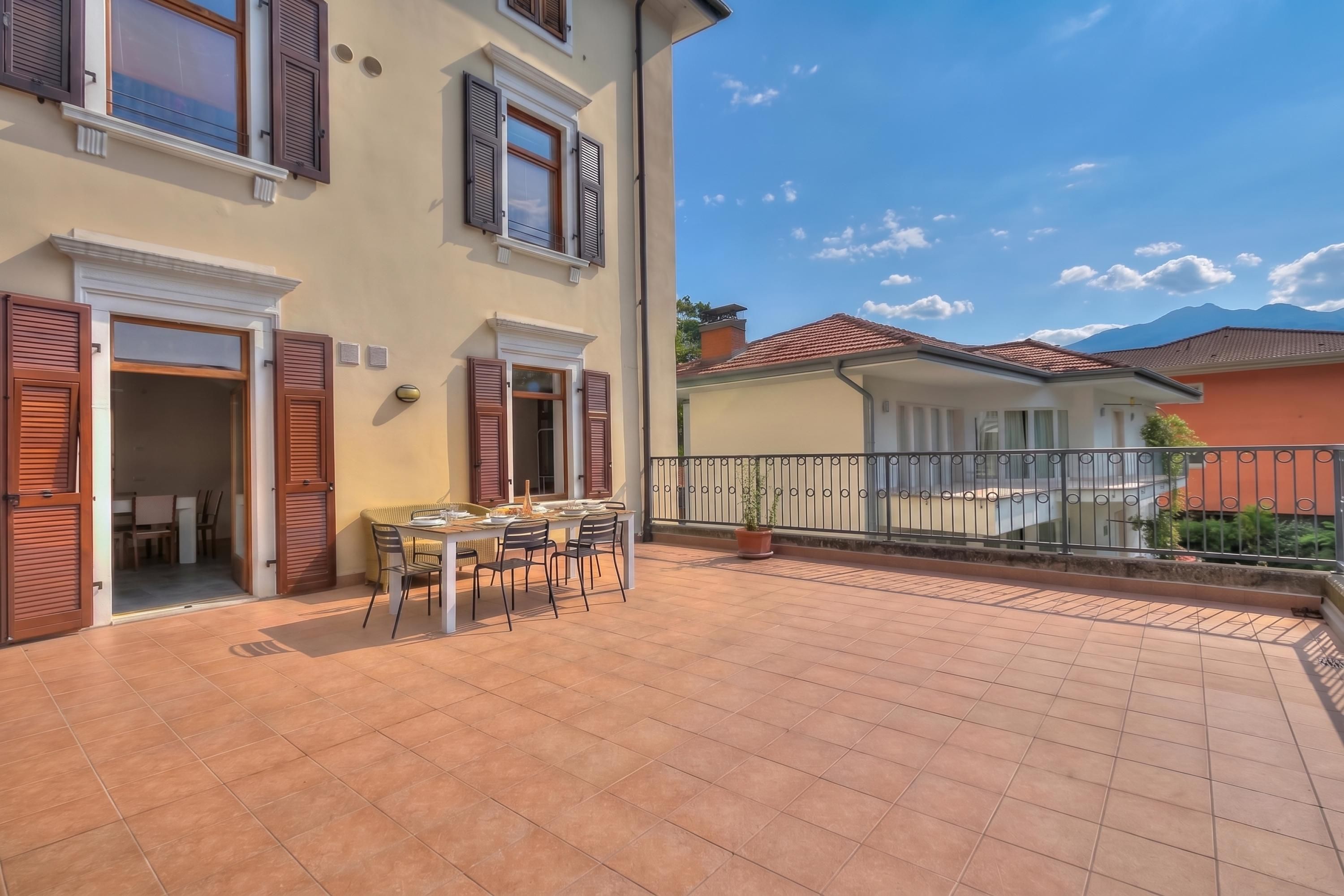 Un immeuble résidentiel doté d’un patio comprenant une table et des chaises, d’un balcon avec une balustrade et offrant une vue sur une montagne en arrière-plan.