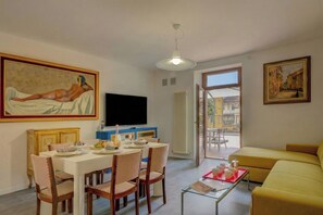Una sala de estar con un sofá, una mesa de comedor con sillas, un televisor y obras de arte en las paredes.