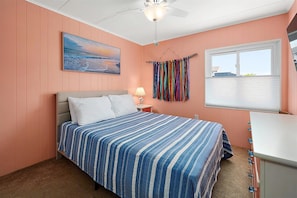Une chambre à coucher avec un lit, une table de chevet, une lampe, une fenêtre et un ventilateur de plafond.