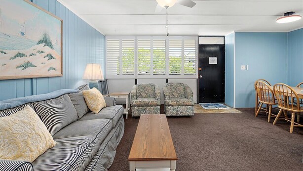 A room with a ceiling fan, a painting, a sofa, two patterned chairs, a wooden table, and a dining set. - Three Bedroom Oceanside Condo Steps from the Beach (Ocean City)
