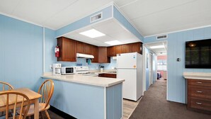 A compact kitchen with wooden cabinets, a microwave, a refrigerator, and a dining area with a wooden table and chairs. - Three Bedroom Oceanside Condo Steps from the Beach (Ocean City)