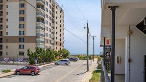 A multi-story building with balconies, a parking lot with cars, and a clear view of the ocean. - Three Bedroom Oceanside Condo Steps from the Beach (Ocean City)