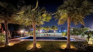 A nighttime outdoor area with palm trees, a pool, and red chairs.