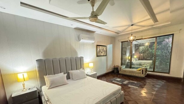 A bedroom with a large bed, two bedside tables, a ceiling fan, a window with a view, and a small seating area by the window.