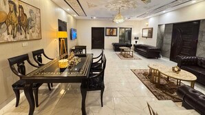 A spacious living room with a black leather sofa, a dining area with a black table and chairs, and a chandelier.