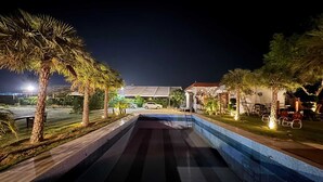 A swimming pool with a tiled edge, surrounded by palm trees and a wooden deck.