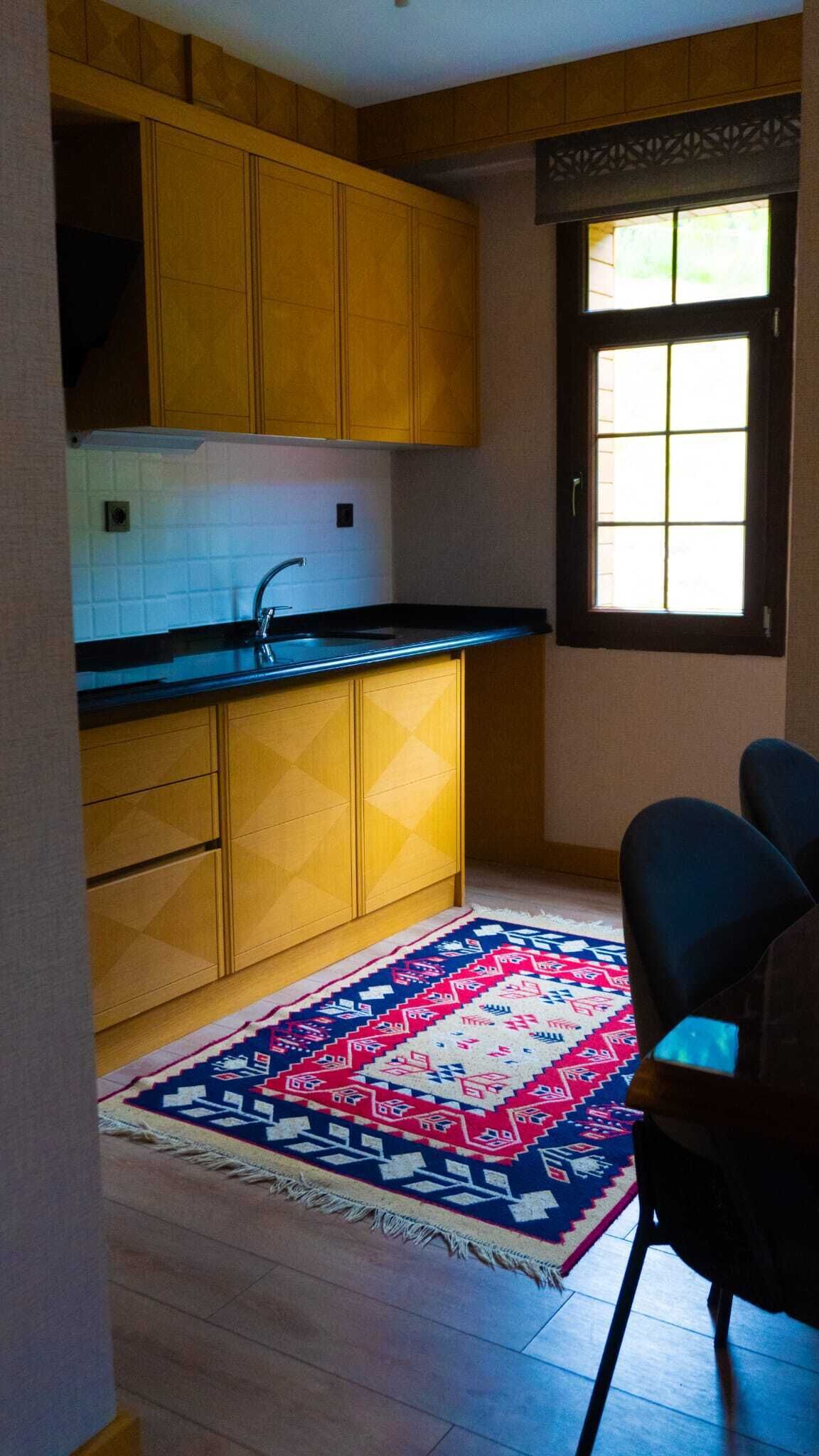 Une petite cuisine avec des meubles en bois, un plan de travail noir et une fenêtre à carreaux.