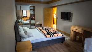 A bedroom with a bed, a wooden nightstand, a wooden dresser, a mirror, and a TV on the wall.