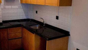 A compact kitchen with wooden cabinets, a black countertop, and a tiled backsplash.