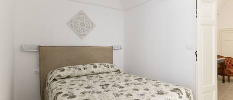 A bedroom with a bed, a headboard, a wall-mounted light fixture, and a door leading to another room.