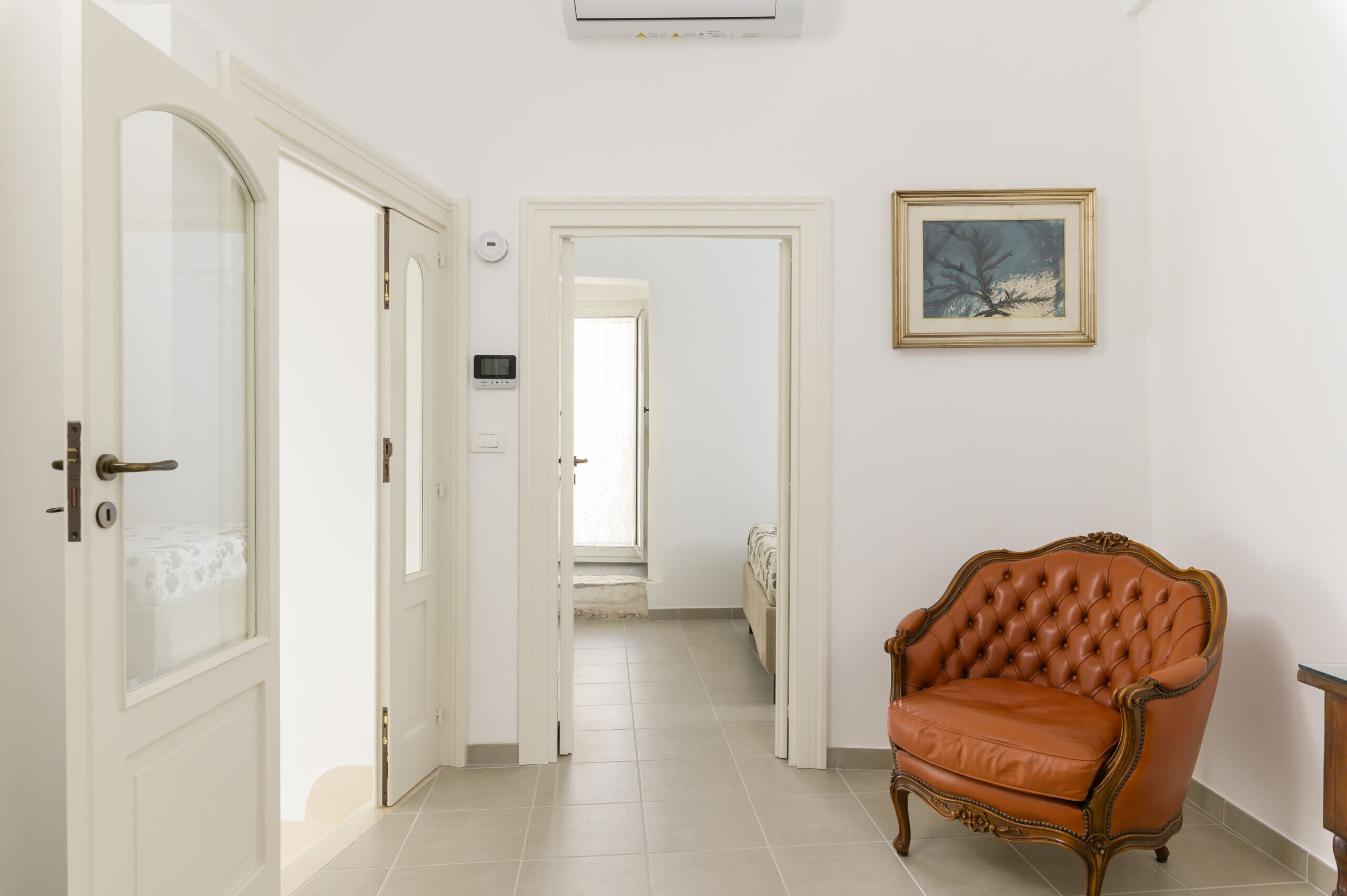A hallway with a brown leather armchair, white doors, and a framed picture on the wall.