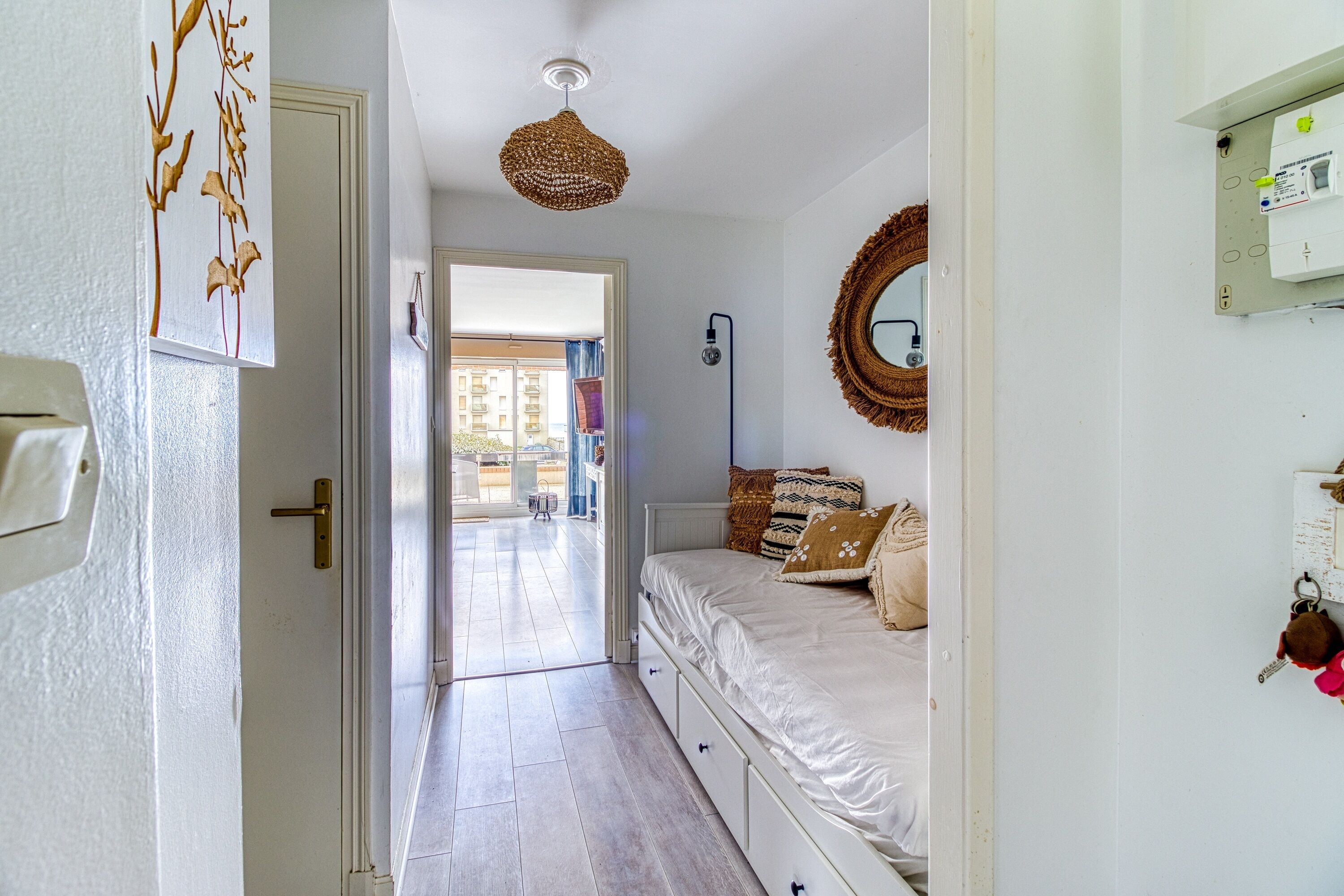 A bedroom with a bed, bedside table, wall-mounted mirror, and a door leading to a balcony.