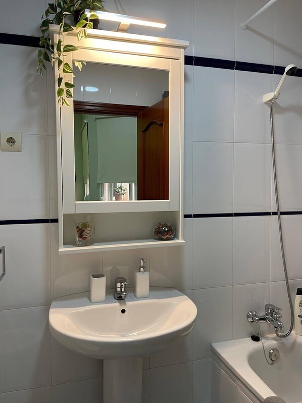 A bathroom with a white sink, a mirror, a shower, and a shelf with toiletries.
