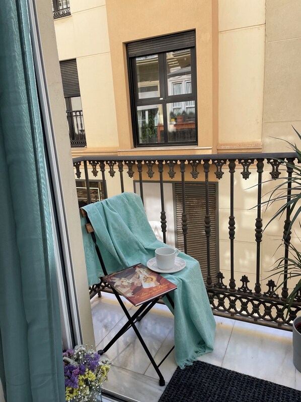 Un balcón con una mesa, una silla, una planta en maceta y una ventana con vistas a la calle.