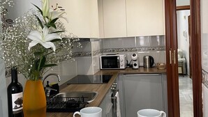 A modern kitchen with white cabinets, a microwave, a kettle, and a sink. There is a vase with flowers on the counter.