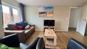 A living room with a sofa, a coffee table, a TV, and a painting on the wall. - Nice apartment for 6 guests with WIFI, TV and terrace (Veere)