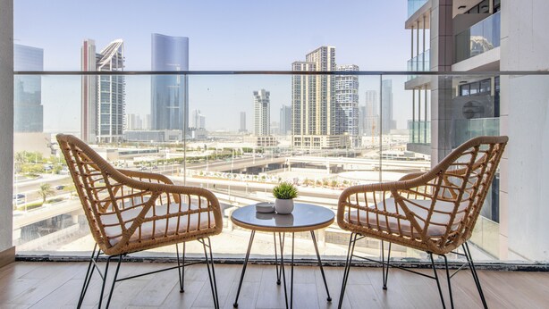 A balcony with two wicker chairs and a small table, overlooking a cityscape with modern buildings. - Bloomfeilds Tranquil STU Al Maryah Vista (Abu Dhabi)