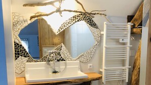 Une salle de bain avec un miroir en forme de cœur, un lavabo blanc et une étagère en bois.