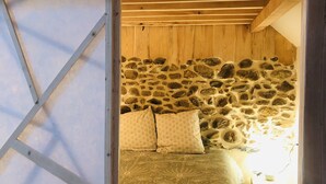 Une chambre confortable avec un mur en pierre, un lit recouvert d’une literie à motifs et une petite table de chevet avec une lampe.