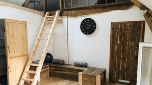Une chambre à coucher aménagée dans un grenier, avec une échelle en bois, une horloge murale ronde, un banc et une porte en bois.