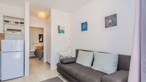 A modern living room with a grey sofa, a white refrigerator, and a small dining area. - Holiday home Korbar (Vir)