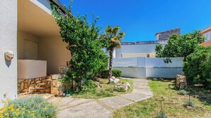 A courtyard with a stone staircase leading to a door, surrounded by greenery and a clear blue sky. - Holiday home Korbar (Vir)