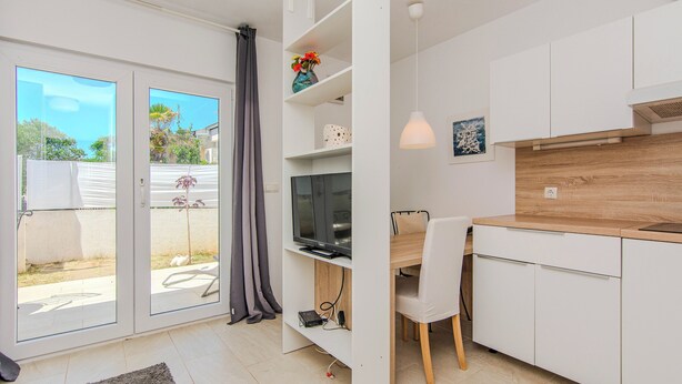 A modern kitchen with white cabinets, a wooden countertop, and a dining area with a white chair. - Holiday home Korbar (Vir)