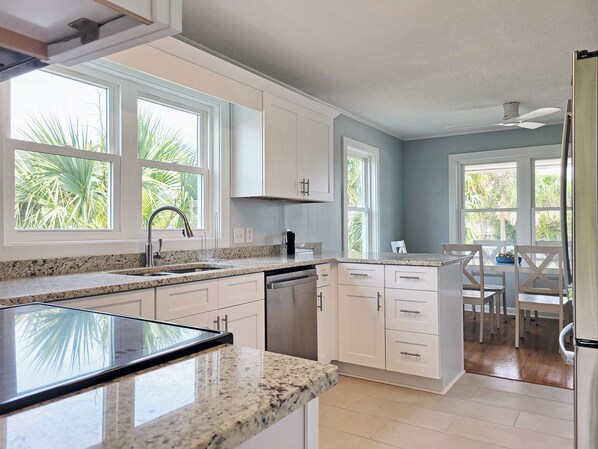 A kitchen with white cabinets, granite countertops, a dishwasher, and a dining area with a table and chairs.