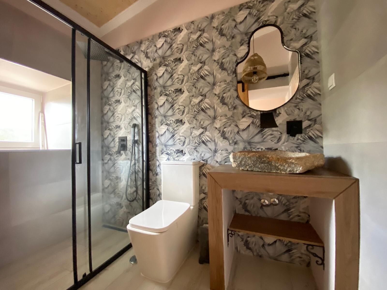 A bathroom with a glass shower door, a toilet, and a vanity with a mirror and a decorative stone.