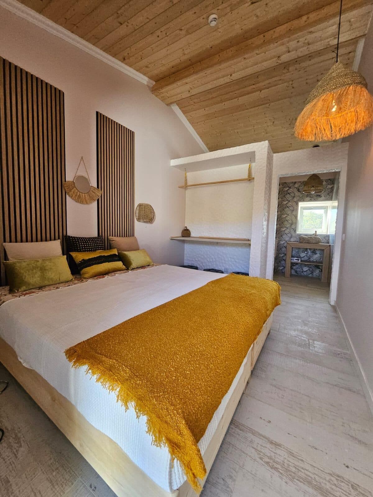 A bedroom with a large bed, wooden ceiling, and a hanging light fixture.