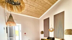Une chambre avec un plafond en bois, un lit recouvert d’une courtepointe blanche et jaune, et un luminaire suspendu.