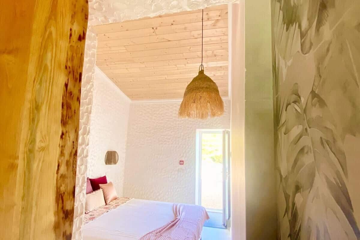 A bedroom with a bed, a hanging light fixture, and a view of the outdoors.
