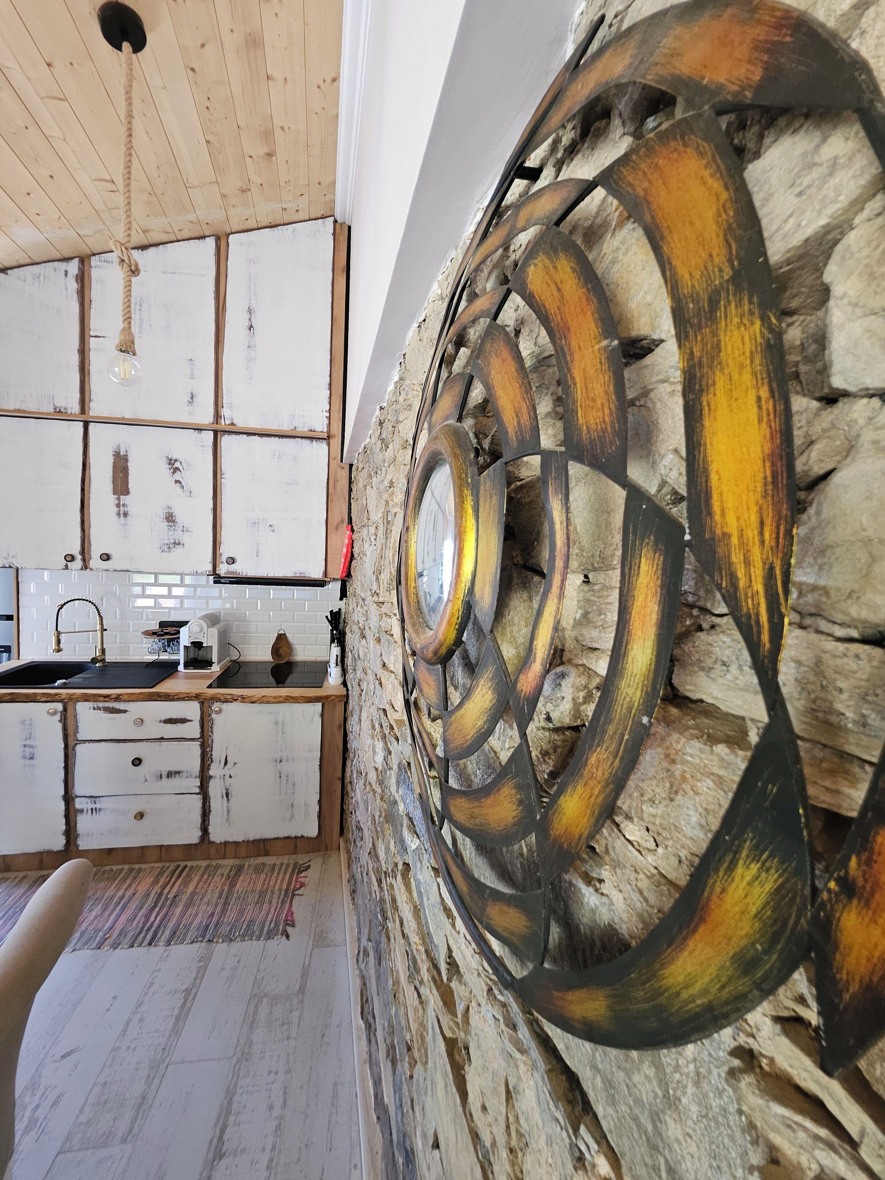 Una cocina rústica con pared de piedra, armarios de madera y una lámpara colgante.