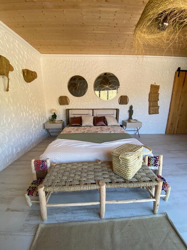 A bedroom with a bed, two nightstands, a woven bench, and a hanging basket.