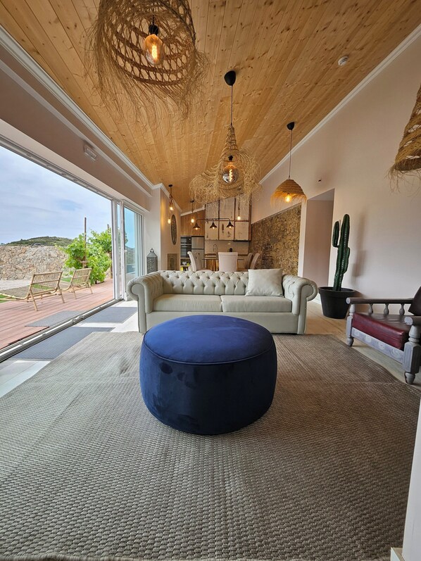 Un salon moderne avec un grand pouf rond, un canapé beige et un coin repas agrémenté d’un mur en pierre.