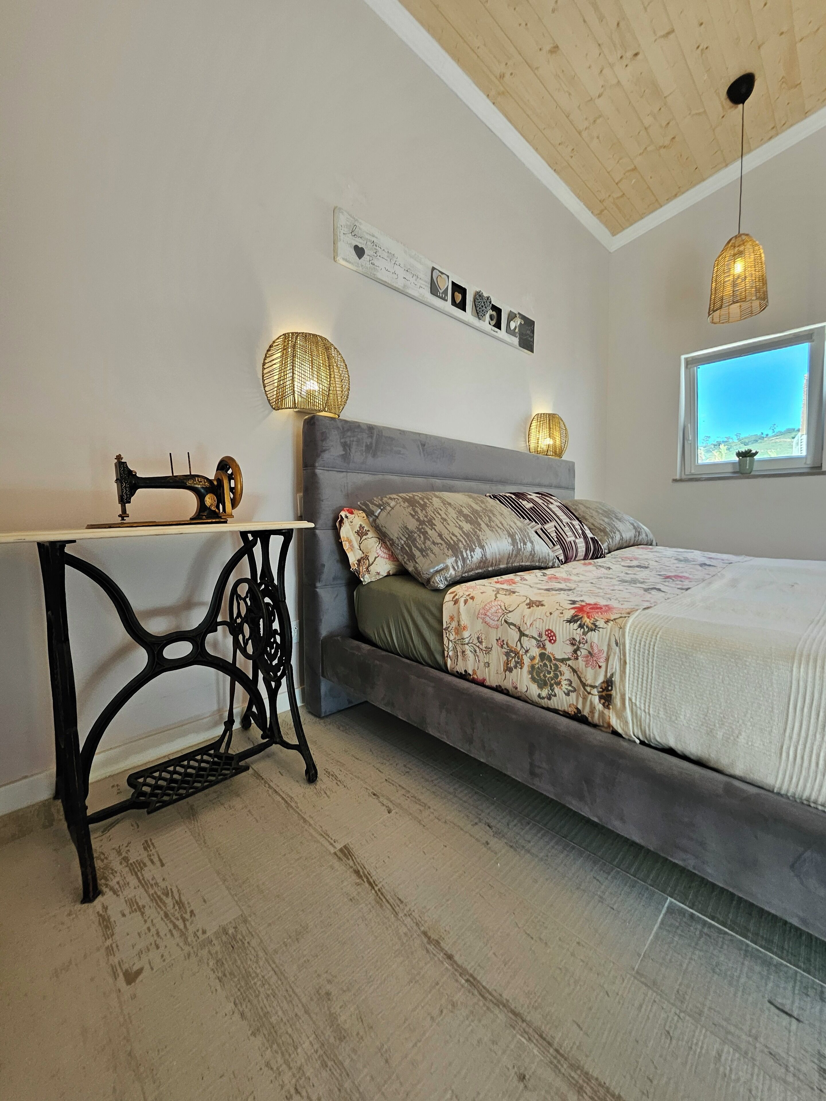 A bedroom with a bed, a sewing machine, and a window with a view.