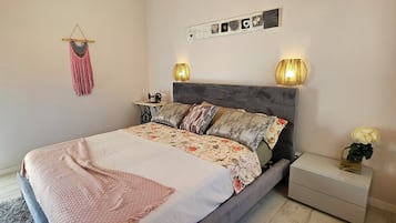 A bedroom with a wooden ceiling, a bed with floral bedding, two bedside lamps, and a small nightstand with a vase of flowers.