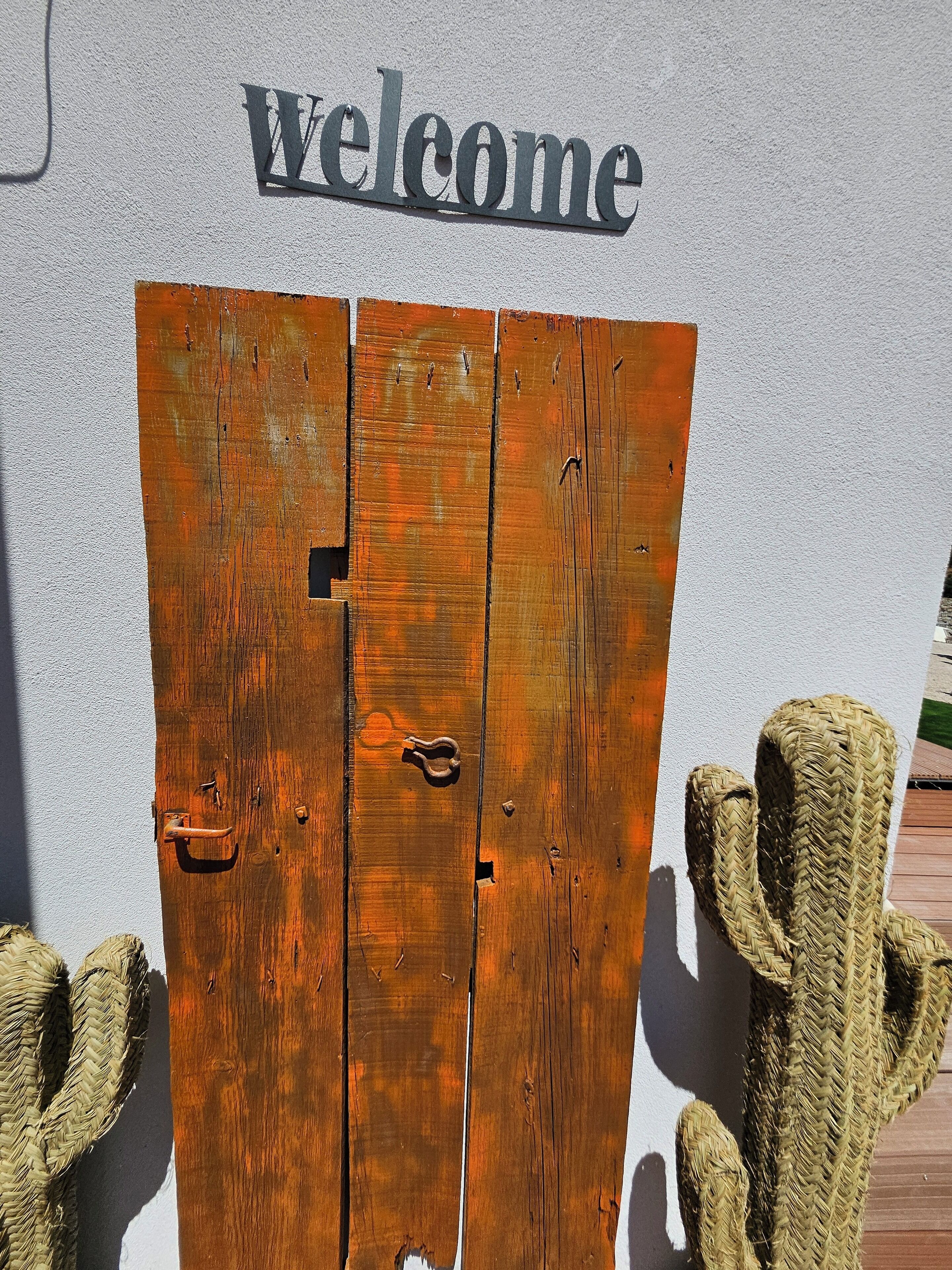 A rustic wooden gate with a 'welcome' sign above it, set against a white wall.