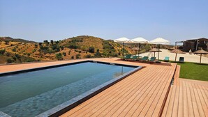 Une piscine avec une terrasse en bois, des chaises longues et des parasols.
