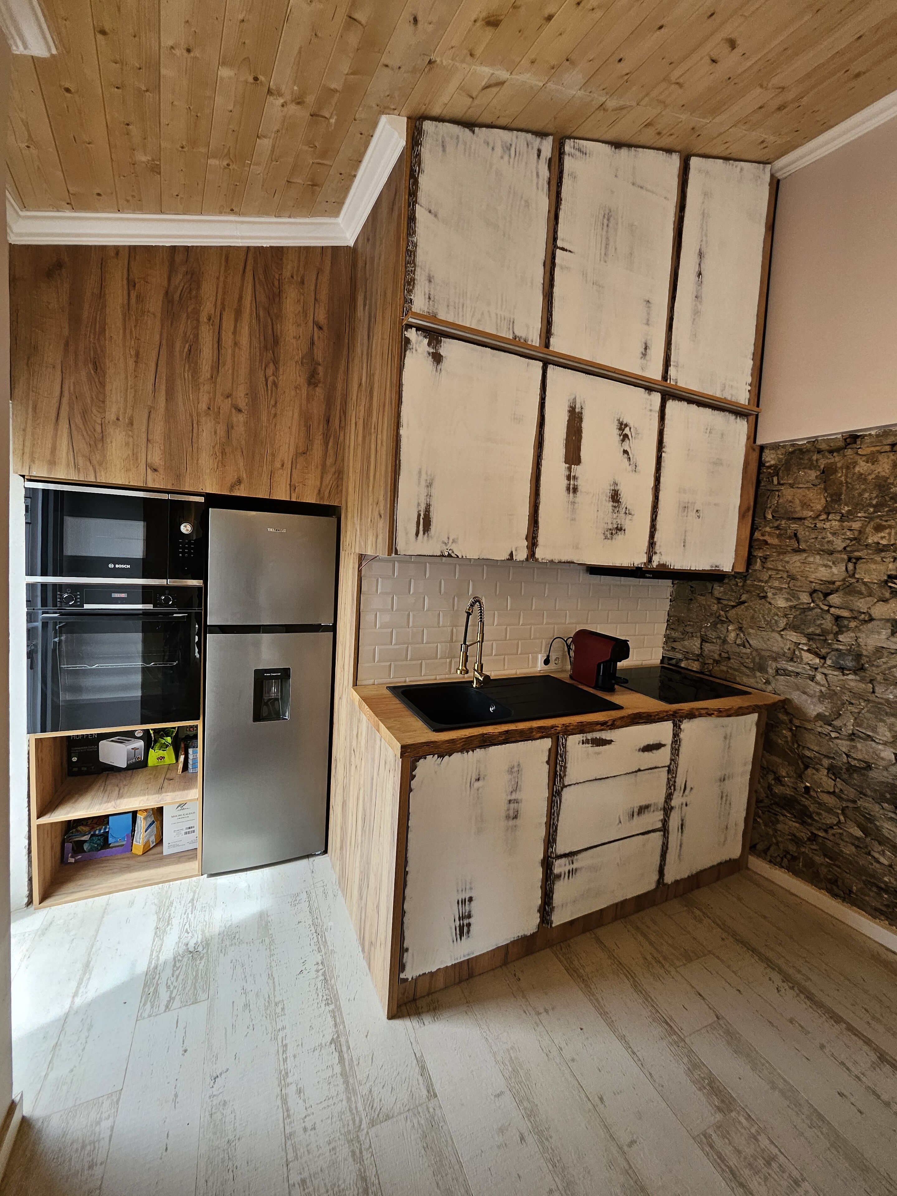 Une cuisine avec des meubles en bois, un réfrigérateur en acier inoxydable et un mur décoratif en pierre.