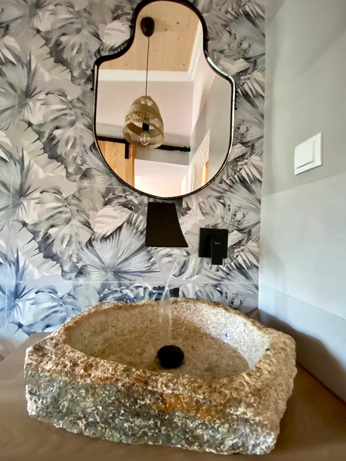 A bathroom with a stone sink, a mirror, and a floral wallpaper.